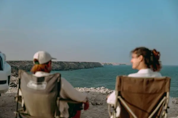 Two people sitting in camping chairs facing the sea in Oman.